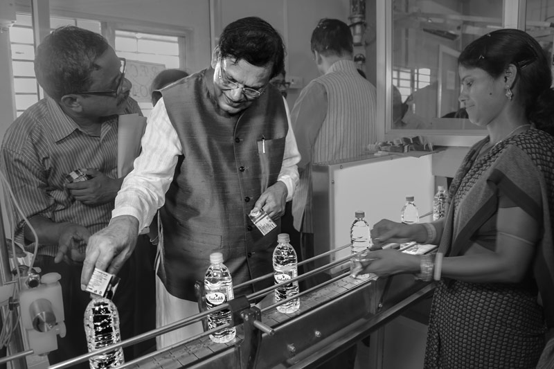 Dr. Pathak trying his hand at fixing brand labels on Sulabh Safe Drinking Water bottles at the automatic rinsing, filling and capping (RFC) unit in Panchberia village, Paschim Medinipur district, West Bengal